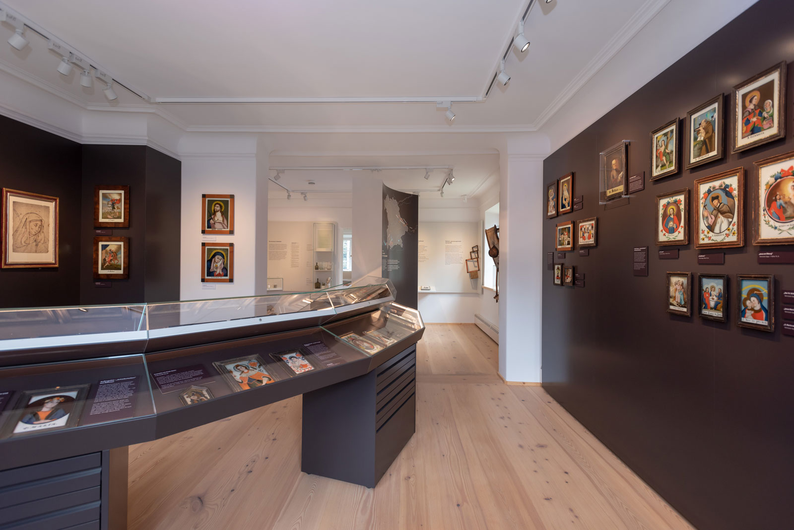 Das Referenzbild für Ausstellungsgestaltung aus der Dauerausstellung Seehausen und der Staffelsee zeigt eine Gemäldegalerie und Schauvitrinen mit Hinterglasmalerei.