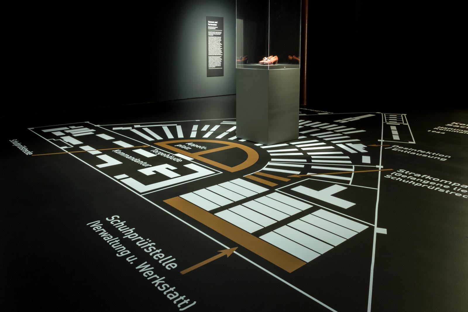 Das Referenzbild für Ausstellungsgestaltung aus der Sonderausstellung „Glanz und Grauen. Mode im Dritten Reich“ zeigt Vitrinen und eine Raumgrafik.