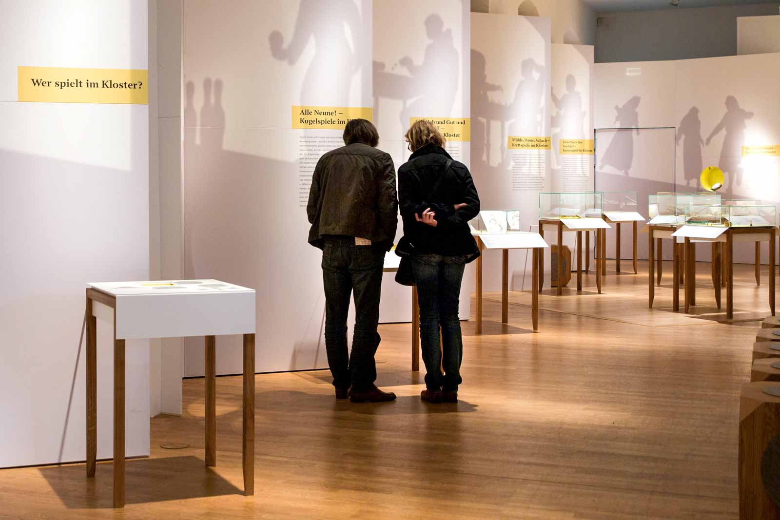 Das Referenzbild für Ausstellungsgestaltung aus der Sonderausstellung „Heiter bis göttlich. Die Kultur des Spiels im Kloster“ zeigt Raumgestaltung mit Tischvitrinen.