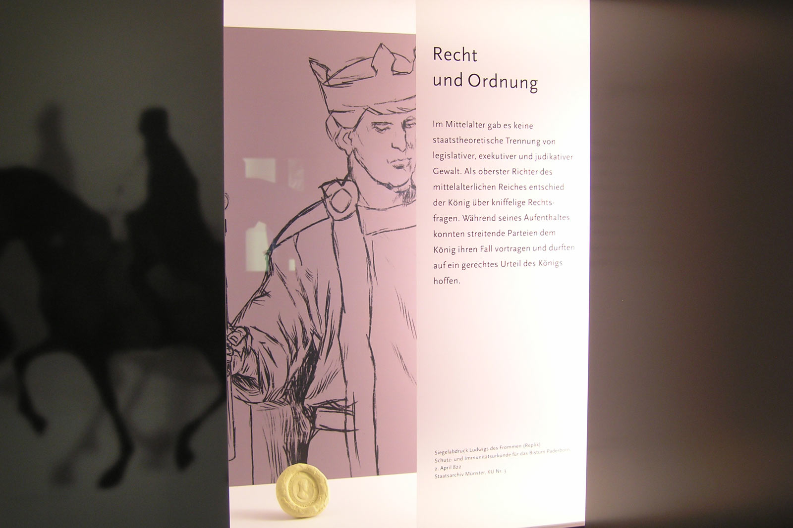 Das Referenzbild für Ausstellungsgestaltung aus der Dauerausstellung „Der Kaiser kehrt zurück“ zeigt eine Exponatpräsentation mit Illustration.