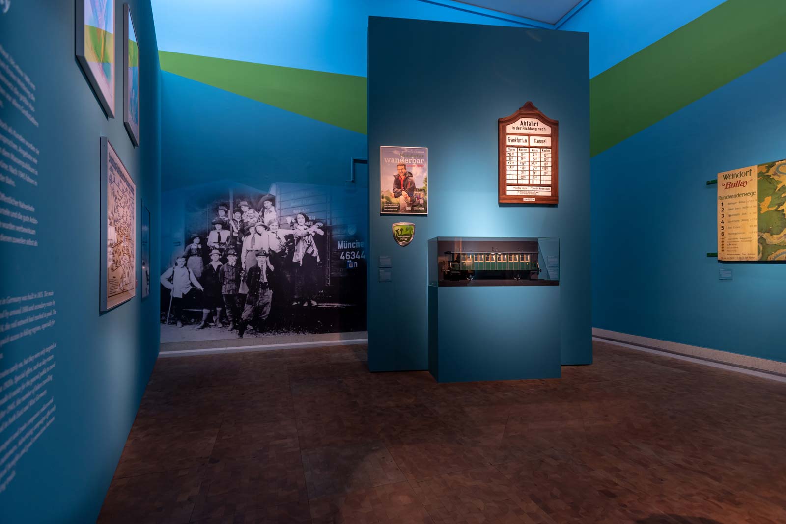 Das Referenzbild für Ausstellungsgestaltung aus der Sonderausstellung Wanderland zeigt eine Rauminszenierung mit Großgrafik und Tischvitrine